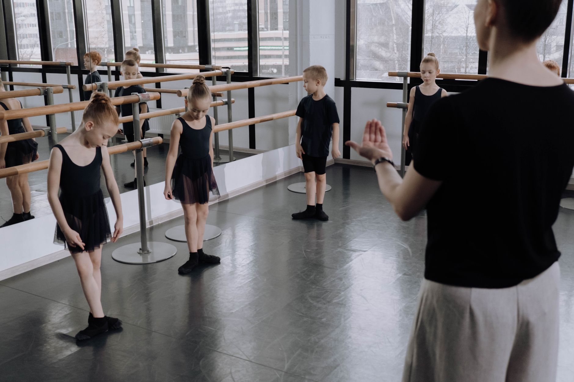 Young ballet students practicing in a bright studio with an instructor guiding them.